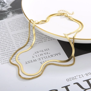 Detail of layered gold snake and box chains on a white plate with artistic magazine background