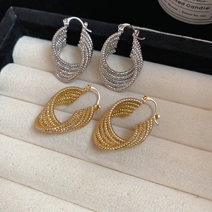 Macro detail of gold and silver twisted oval hoop earrings in a beige velvet jewelry box