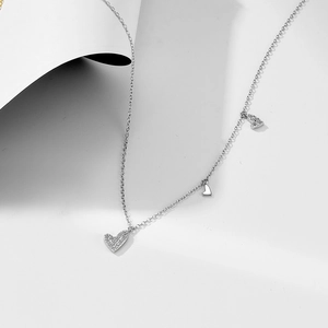 Macro detail of silver necklace featuring triple heart pendants with shimmering crystals
