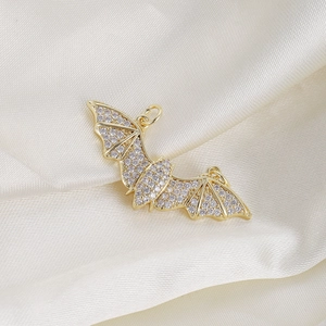 Detailed view of a gold-plated bat pendant with pavé cubic zirconia on silk background