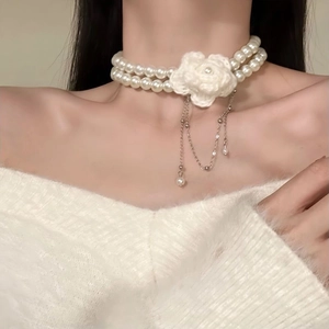 Detail of double-layer pearl choker with hand-knitted flower and metallic fringe tassels