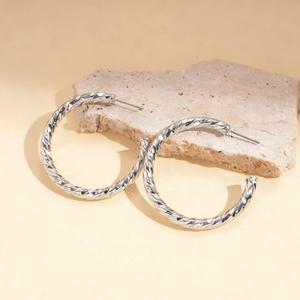 Close-up of silver geometric C-shape hoop earrings with twisted texture on a stone