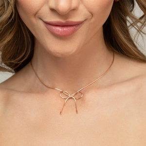 Close-up of rose gold bow pendant necklace on a delicate snake chain worn by a model