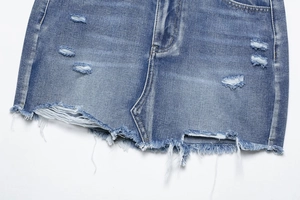 Detail shot of distressed blue denim skirt featuring ripped holes and raw fringe edges