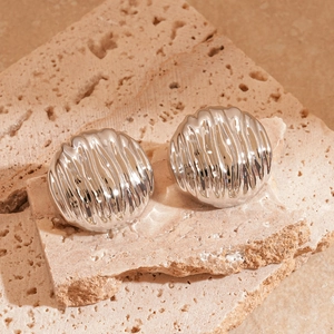 Gros plan sur des boucles d'oreilles rondes argentées plissées sur pierre beige