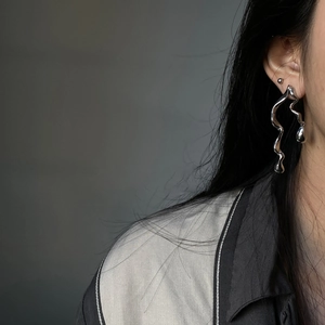 Macro shot of liquid metal style asymmetrical wavy earrings on model in cool grey setting