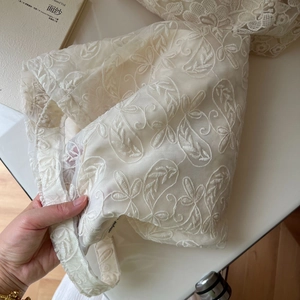 Close-up of ivory lace embroidery fabric with delicate floral patterns and woven lace edges