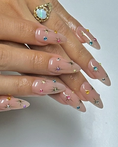 Long almond press-on nails in nude pink with golden stars and colorful gemstones