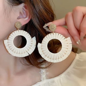 Detail of bohemian round white raffia earrings worn by a model for a resort beach look