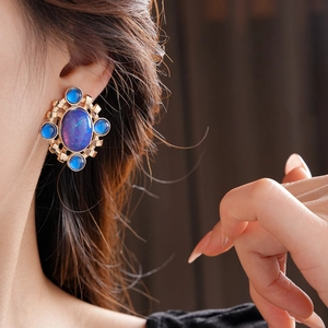 Macro detail of a vintage gold-tone earring with a blue opal stone worn by a model