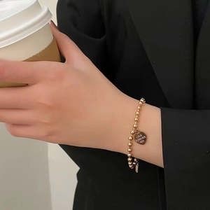 Minimalist gold beaded titanium steel bracelet with engraved heart charm on woman's wrist