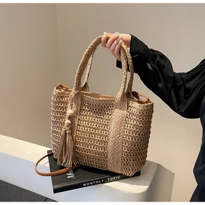 Detail of khaki straw tote bag featuring woven texture with tassel charm and leather strap