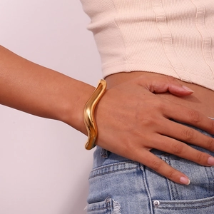 Detailed view of irregular wavy 18K gold-plated stainless steel cuff on female wrist