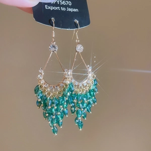 Detailed macro of gold drop earrings with emerald crystals and layered tassels
