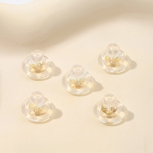 Detailed macro view of five 18K gold and clear silicone earring backs on beige background