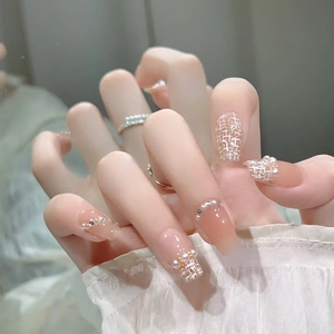 Close-up of nude pink press-on nails with luxury tweed patterns, pearls, and rhinestones