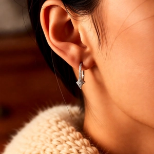 Close-up of silver star earrings with pavé zircons worn by a model in a beige sweater