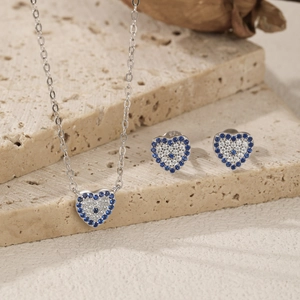 S925 silver heart jewelry set with blue devil eye crystals on beige stone background