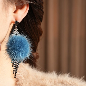 Macro view of blue fur pom pom earrings with sparkling rhinestones worn by a model