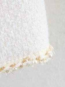 Dettaglio macro del tessuto tweed bianco con rifiniture in perle e filo dorato intrecciato