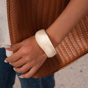 Detail of cream resin bangle with marble texture paired with a brown woven bag