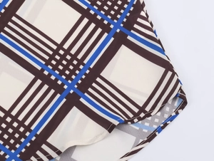 Detailed macro shot of curved hem stitching on blue and brown plaid chiffon shirt