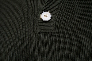 Macro shot of dark green ribbed knit texture with a high-quality four-hole resin button