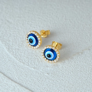 Close-up of blue evil eye stud earrings with cubic zirconia halo in gold plating