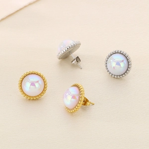 Elegant gold and silver twisted pearl stud earrings with colorful luster set on beige fabric