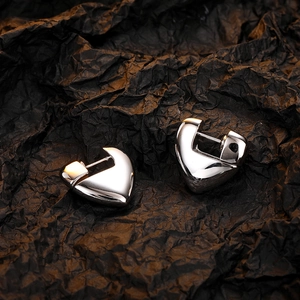 Detailed view of polished silver heart-shaped earrings on a textured black background