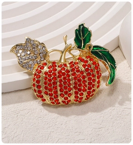 Detailed view of a golden pumpkin brooch with red rhinestones and green enamel leaves