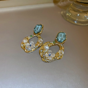 Détail des boucles d'oreilles fleurs dorées avec gemme bleu sarcelle et cristaux brillants