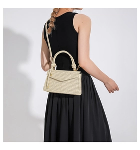 Detail of woven beige crossbody bag with gold hardware and knot handle detail on model