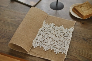 Macro detail of natural jute placemat featuring delicate white floral lace trim on wood