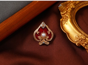 Macro detail of gold spade brooch with red enamel, pearl inlay and rhinestones