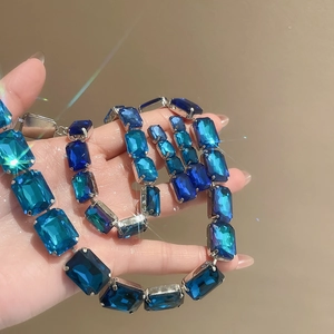 Macro shot of a hand holding luxury silver necklace and square blue crystal earring set