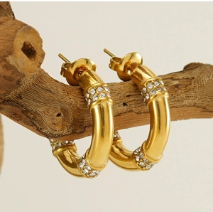 Macro view of gold-plated bamboo hoop earrings with crystals on a wooden branch