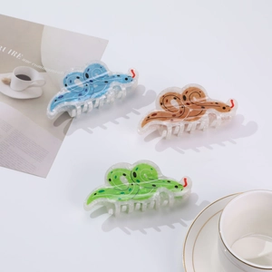 Three snake-shaped hair claws in blue, brown, and green acrylic on a white table