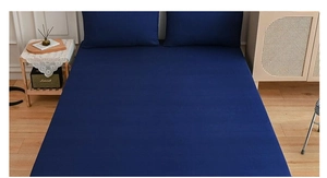 Detail of dark blue fitted sheet and two pillowcases in a cozy bedroom setting