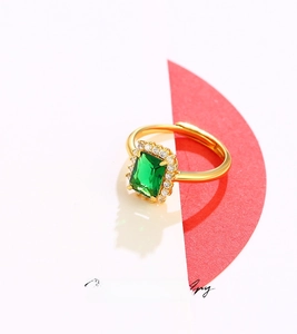 Detailed macro view of a gold-toned ring featuring an emerald-cut green gemstone and halo