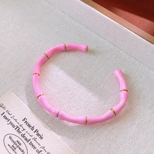 Dettaglio del bracciale smaltato rosa stile bambù con accenti dorati su vassoio in legno