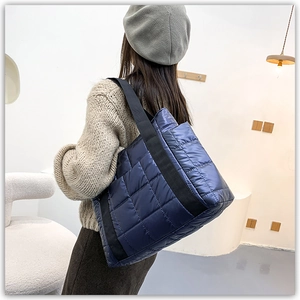 Detail of dark blue quilted puffer bag with glossy finish and wide textile shoulder strap