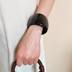 Close-up of a wide black acrylic bangle with a geometric design worn on a woman's wrist