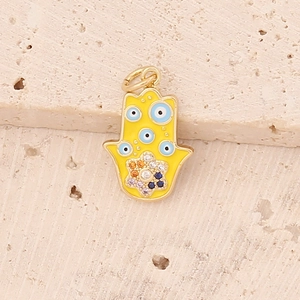 Detail of yellow enamel Hamsa hand pendant with blue evil eye motifs and zircon inlay
