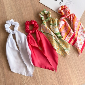 Close-up of four satin bow scrunchies with long ribbons on a wooden background