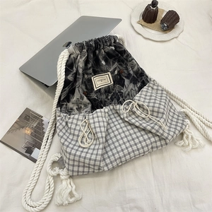 Flat lay of a plaid drawstring backpack with laptop and stationery in a lifestyle scene