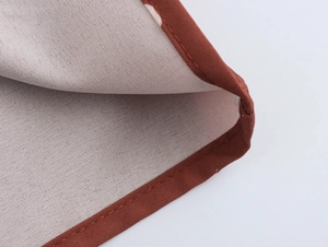 Vue détaillée du tissu beige avec bordure rouge brique et finitions à double couture