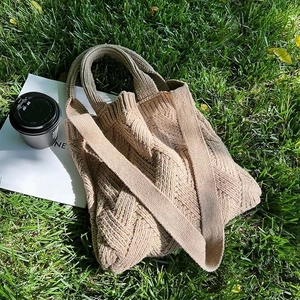 Close-up of beige knitted tote bag with woven texture on grass with coffee and magazine