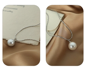 Close-up of elegant silver necklace with a large pearl pendant on beige silk background