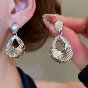 Silver hollow teardrop earrings with radial texture shown being worn and held by hand